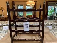 Front view of a dark wooden wine rack with three shelves and scalloped slots for 12 bottles. Features decorative finials on four corner posts.