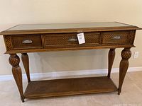 Front view of the buffet table showing three rattan front drawers with shell-style metal handles and glass top.