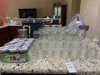 Image showing canning jars of various sizes arranged on a countertop with speckled black canning pot in background.