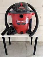 Front view of red Craftsman shop vac with hose attached and multiple nozzle attachments displayed in front.