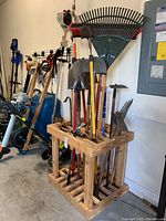 Various garden tools stored in wooden rack, including shovels, hoes, rakes, and a broom