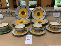 Front view of 14-piece Ecuadorian hand painted dinner set with colorful plates, bowls, cups and saucers arranged on counter.