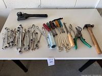Overview of all hand tools on white table including wrenches, screwdrivers, pliers, hammer and hacksaw