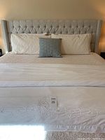 Full view of king size bed with upholstered tufted headboard and nailhead trim, with bedding and pillows, showing overall condition and style.