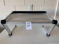 Front view of silver aluminum ventilated laptop desk stand showing Z-shaped adjustable legs with pivot joints and black rubber stop bar.