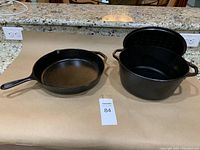 Photo showing black Lodge cast iron frying pan and Dutch oven on countertop with tag number 84.