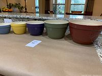 Side view of six nested colorful ceramic mixing bowls in descending sizes and colors (gray, yellow, blue, olive green, rust red)
