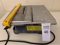 Side view of QEP 7-inch wet tile saw showing yellow guard, metal cutting surface, power cord, and label with specifications