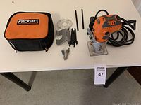 Ridgid plunge router with accessories and soft case arranged on table.