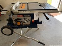 Front view of Ryobi table saw on silver folding stand with wheels, blade installed