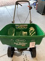Front view of the Scotts Turf Builder EdgeGuard DLX broadcast spreader showing green hopper with brand and model labeling.