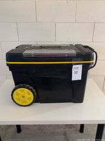 Side view of the Stanley tool chest showing its large yellow wheels and black plastic body with scratches.