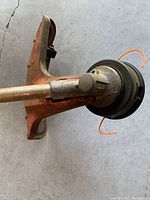 Close-up of the weed eater's nylon line cutting head and rust-colored protective guard, showing wear and some rust.
