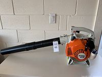 Side view of Stihl BG55 leaf blower showing the orange engine casing, white handle, black nozzle, and MaxSold auction tag.