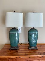 Pair of matching porcelain table lamps with blue-green gradient bases and off-white fabric shades on wooden table.