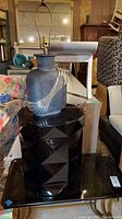 Full view showing metal art deco style lamp sitting atop the black acrylic geometric side table, both on glass surface