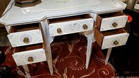 Front and side angles of the antique painted vanity table with drawers open, showing painted floral details and brass hardware.