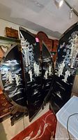 Four black lacquered wooden panels of the Asian room divider, shown standing and partially extended, showcasing the detailed carved and enameled brushwork with figures and architectural motifs.