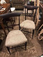 Pair of wooden chairs with dark frames and chevron upholstered seats arranged side by side on a carpeted floor.