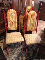 Two wrought iron chairs with red metal frames, upright tall backs with decorative scrolls, and upholstered seats and backs in a patterned fabric indoors on a rug.