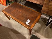 Top and side angle view of the coffee table showing brown tile surface and wood frame with legs.