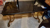Full front perspective of coffee table showing glass top resting on brass base with rounded edges on glass and curved legs touching floor with paw ends.
