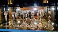 8 crystal candlestick holders displayed on a glass shelf including various shapes and styles with clear crystal and cut designs.