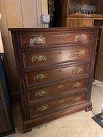 Front view of the dark wood dresser showing six drawers with ornate metal handles and visible wear.