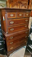 Front view of the vintage wooden tallboy dresser showing 8 drawers with brass handles and visible wear.