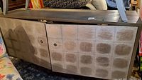 Front view of entertainment cabinet showing metallic enameled grid pattern doors and painted wood top, placed on a carpeted floor.
