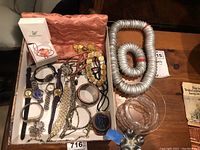 Photo showing assortment of wristwatches, bracelets, chains, a long necklace made of bottle caps coiled, a clear plastic item, and a Swarovski jewelry box.
