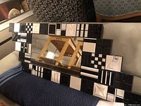 Overall view showing rectangular mirror with a thick decorative frame made up of black and white tiles with geometric patterns.