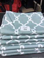 Stacked blue curtain panels with white geometric trellis design, folded with a lot number card on top