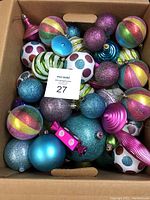 Box filled with various colorful Christmas tree ornaments including glittery, matte, and shiny baubles in multiple colors and patterns.