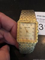 Front angle of square Bulova watch face and textured bracelet showing gold-tone finish and jewel hour markers.