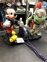 Photo showing both Mickey Mouse and Buzz Lightyear retro telephones on a table, with visible cords and base units.