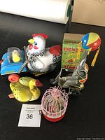 Full view of all five tin type wind-up toys including chicken, duck, robot, small blue vehicle with chick, and pink birdcage with bird