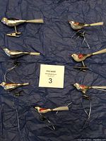 Seven vintage glass bird ornaments laid out on blue fabric, showing their varying poses and attached metal clips.