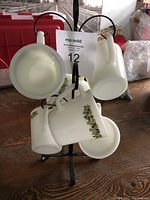 Full view of six white Pyrex mugs hanging on black metal mug stand with floral green trim design