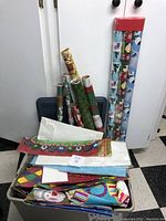 View of multiple rolls of wrapping paper standing behind a filled storage container including gift bags and tissue paper.