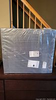 Front view of a sealed package containing multiple square acoustic panels wrapped in clear plastic, showing product labels and shipping tags.