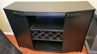 Front view of the black wooden bar cabinet showing the central wine bottle rack and open shelf, flanked by two side cabinet doors.