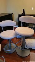 Two beige padded barstools with round seats and backs on metal bases with footrests, showing overall appearance and condition.