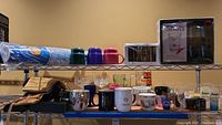 Wide view of shelf with shot glasses, cocktail glasses, stemware, mugs, coasters, Crown Royal bags, and Pepsi cups.