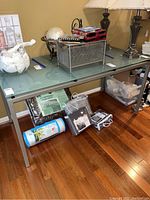 Full view of metal framed desk with frosted glass top and various items placed on and under it (items not included). Hardwood floor beneath.