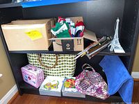 Box with 29 mini stockings in red, green, and white, wooden knitting needles, silver metal Eiffel Tower ornament, blue suede pouch by American Apparel, vinyl woven handbag, pink Hello Kitty first aid kit, two floral beaded change purses, and Vera Bradley mini backpack on shelf.