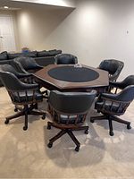 Wide shot of the hexagonal game table surrounded by six matching swivel chairs with black leather upholstery and wooden frames.