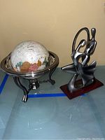 Desk globe with metal stand and abstract metal sculpture on a glass table.