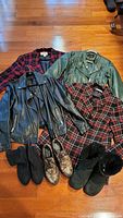 Top-down photo showing all items of clothing and footwear together on floor: two faux leather moto jackets (black and green), two plaid blazers, black Ugg boots, snakeskin-patterned loafers, black ankle booties.