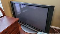 Full view of LG Plasma TV sitting on oval grey base stand beside wooden furniture.